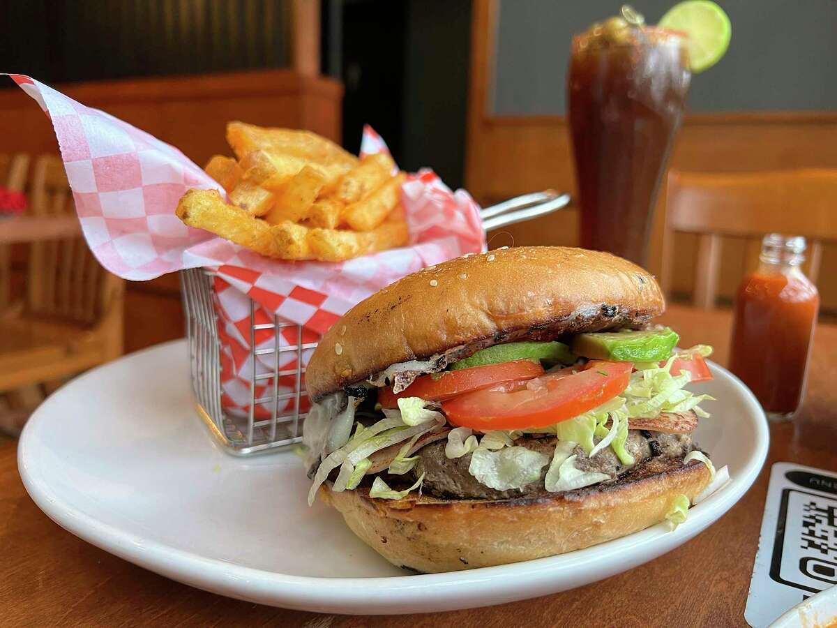 A Mexican hamburguesa includes beef, ham and grilled panela cheese, served with fries at Tu Asador, a Mexican-style steakhouse in Castle Hills. Drinks include a 24-ounce draft Negra Modelo beer dressed as a michelada, background.