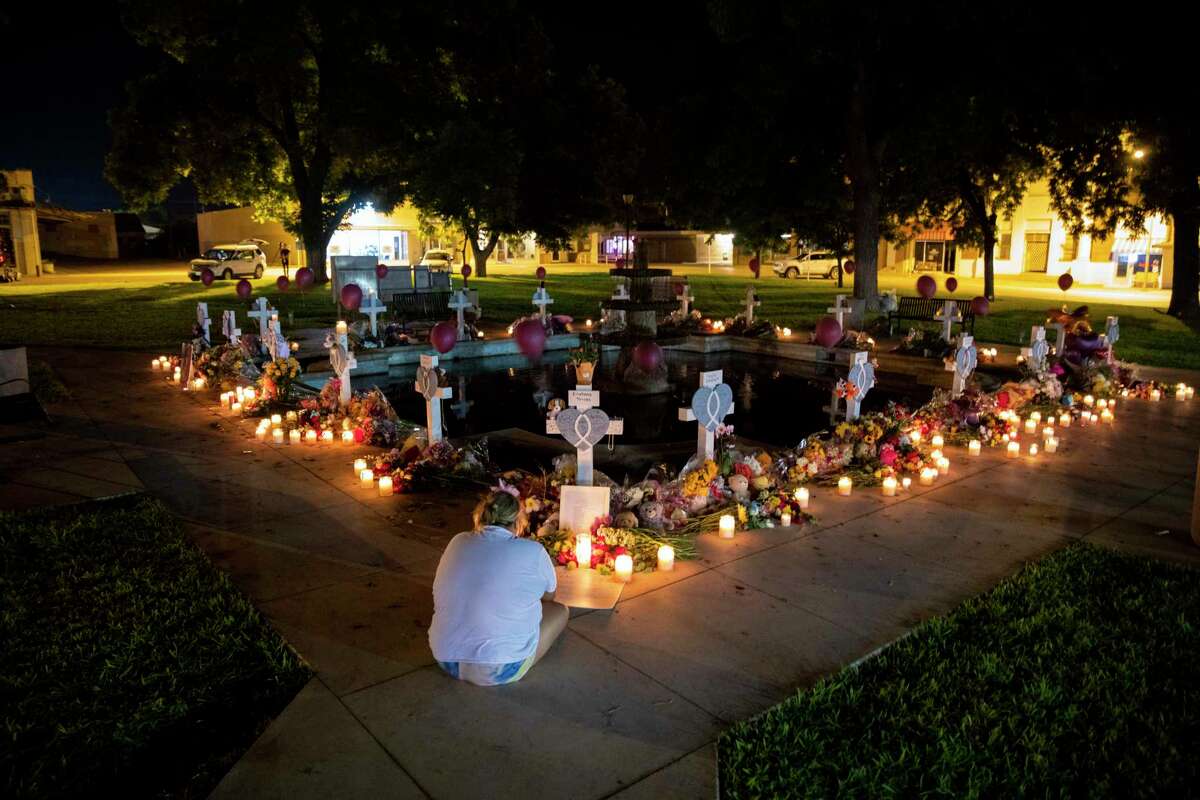 A woman mourns before the 21 crosses bearing the names of the victims of the mass shooting at Robb Elementary School at a memorial set up in the town square in Uvalde, Texas, early Friday morning, May 27, 2022.