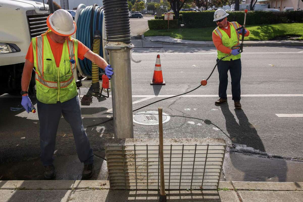 (L to R) Steve Durkee holds the hose in place as Antonio Cerna prepares the water hose to help clean out the drain in Fremont, Calif., Thursday, April 7, 2022.