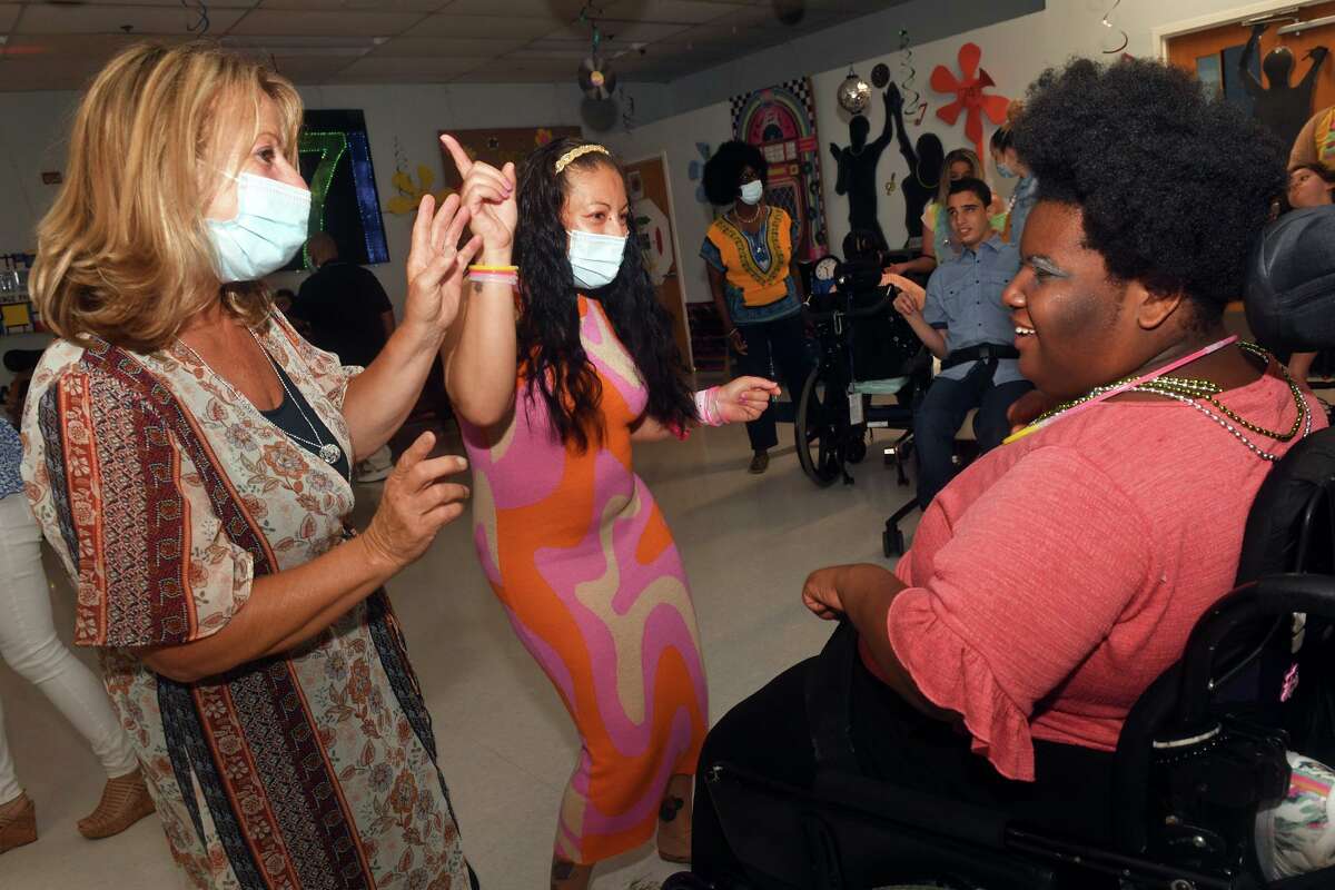 Staff members Dawn D’Angelo, left, and Leslie Gomez, center, dance with Cionee Miles during a disco themed prom held for the students at St. Vincent’s Special Needs Services, in Trumbull, Conn. May 27, 2022.