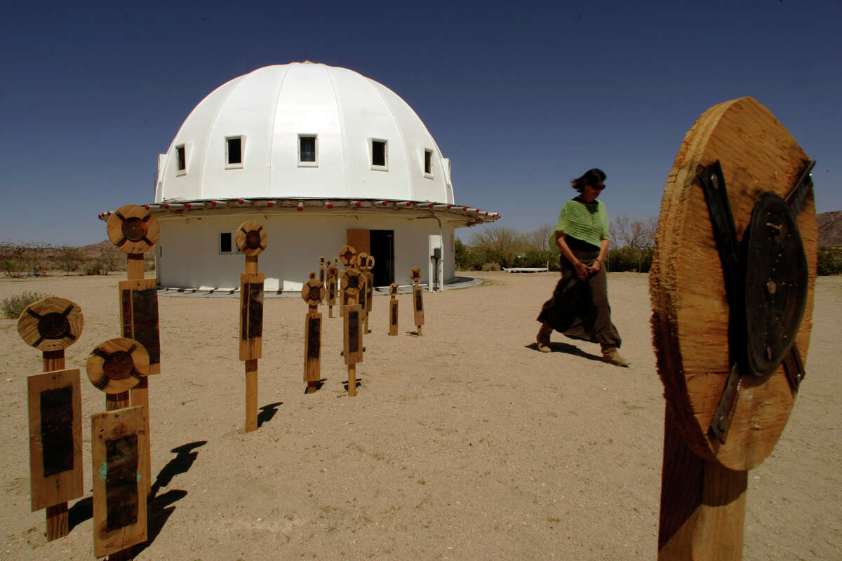 The Integratron stands among "Alien Men", in foreground, created by artist Johnette Napolitano, as Nancy Karl, 48, walks by on right, circa 2006.