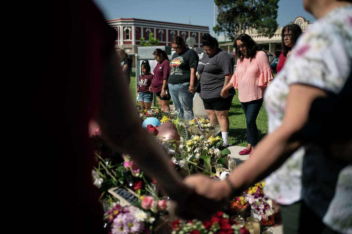Hinojosa McKenzie, 28, fourth from left, prays for her cousin Eliahana Torres and other victims, at a memorial site for victims killed in the Robb Elementary school shooting on Saturday in Uvalde, Texas.