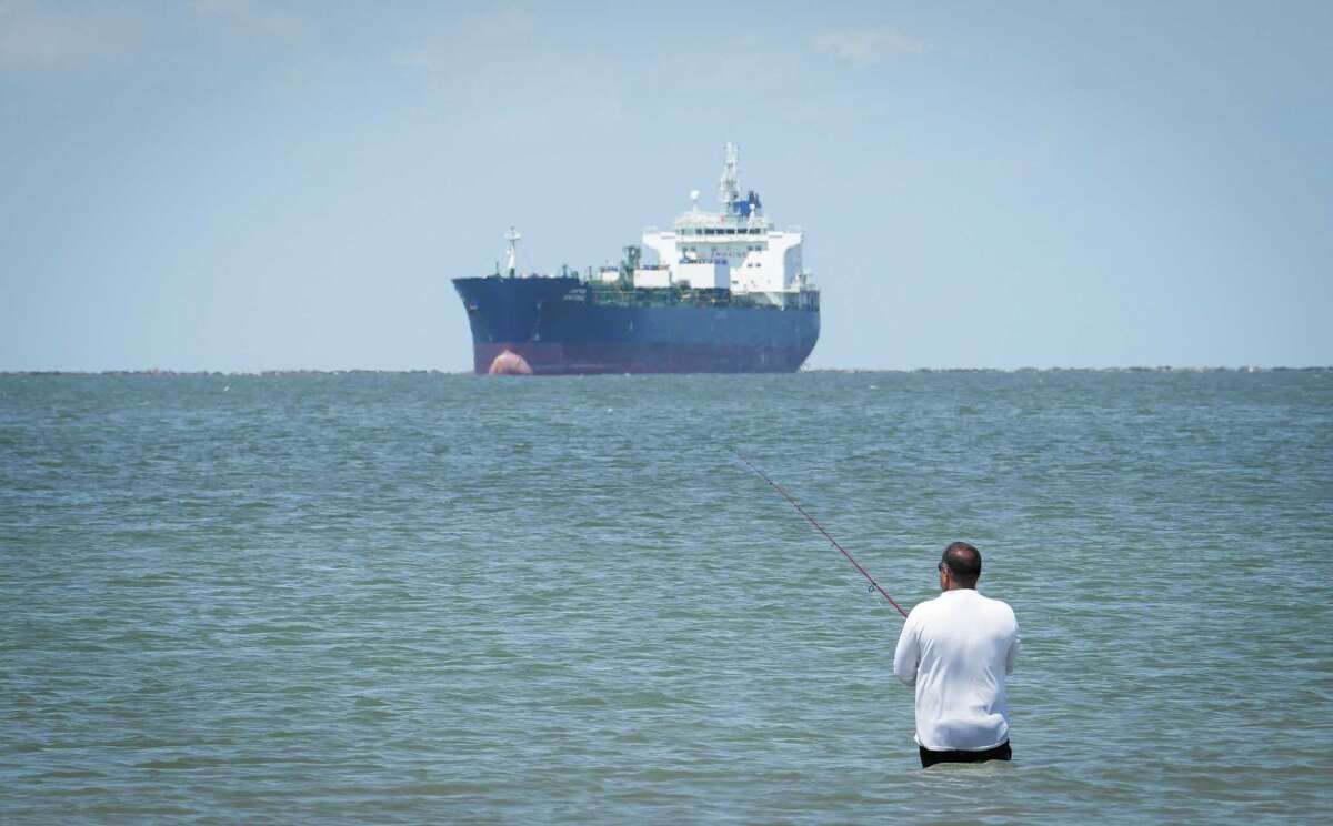 A man fishes as a large ship waits to enter the Houston Ship Channel on Sunday, May 15, 2022, at East Beach in Galveston.