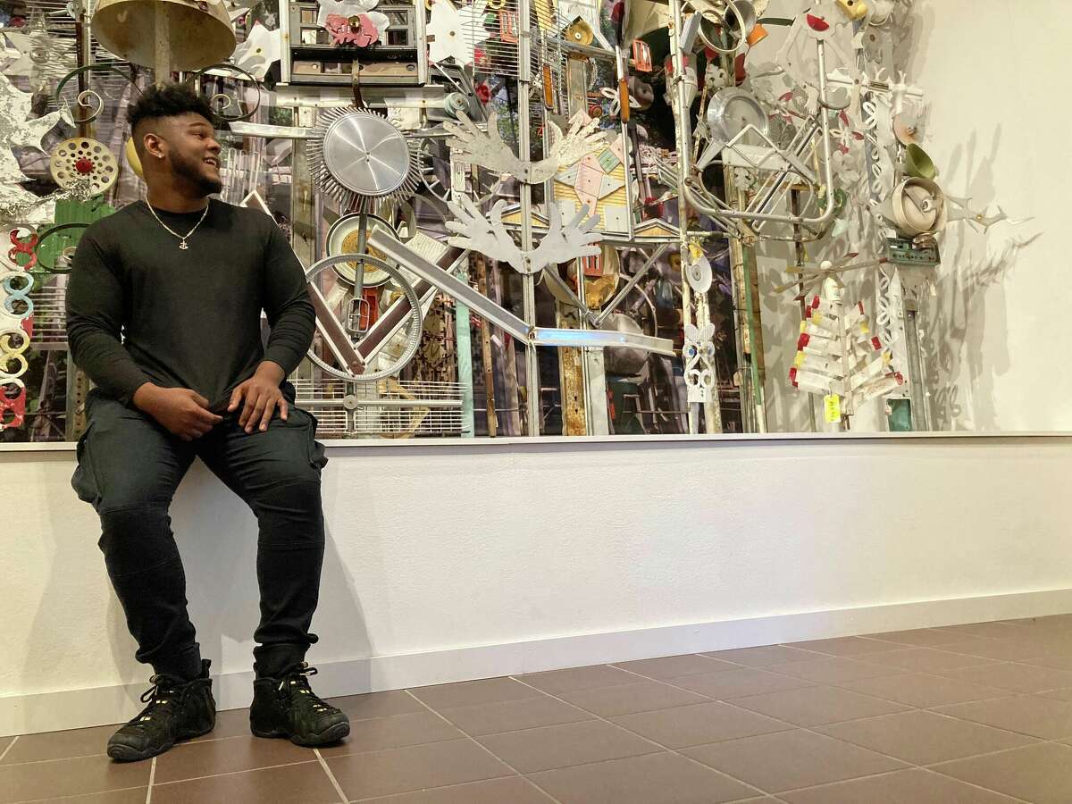 DeAndre Nico sits beside Felix "Fox" Harris' artwork in the Art Museum of Southeast Texas, where he will be performing for First Thursday on June 2.