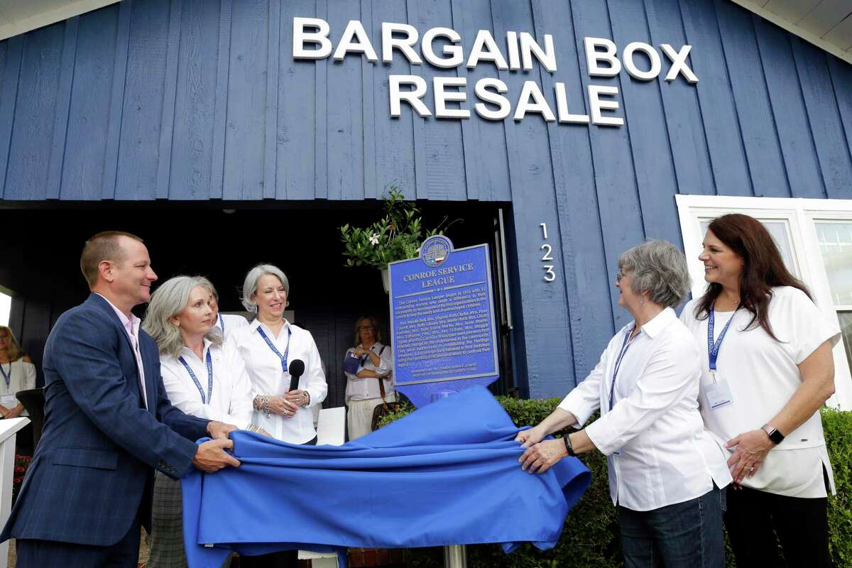 Conroe mayor Cody Csajksoki, left, and other dignitaries remove a blue cloth during an unveiling ceremony for a historical marker by the Montgomery County Historical Commission honoring the Conroe Service League at the Bargain Box Resale Shop Thursday, Oct. 14, 2021 in Conroe.