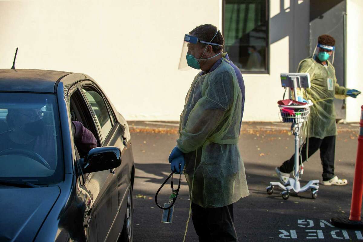 Dr. Brian Hertz, center, talks with patient Walter Kletke of Petaluma as he sits inside his car after receiving a COVID-19 test at Petaluma Health Center in Petaluma, Calif., on Jan. 24, 2022.