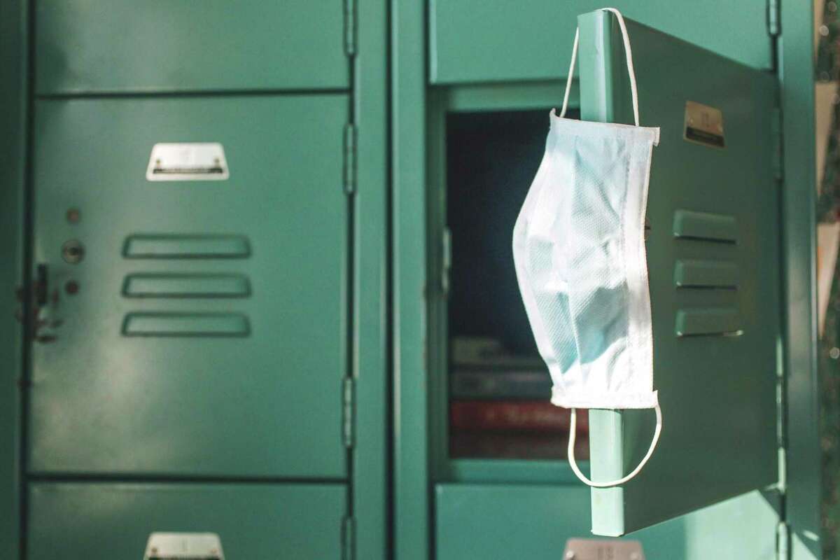 Surgical mask hanging inside school on locker. The number of students and staff infected with COVID-19 is continuing to decline, according to recent state data.