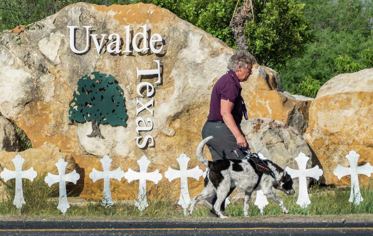 A woman and dog walk by crosses at the city limit of Uvalde on Thursday, June 2, 2022. The crosses were erected to rememberer the 19 students and two teachers who were shot and killed by a gunman on May 24.
