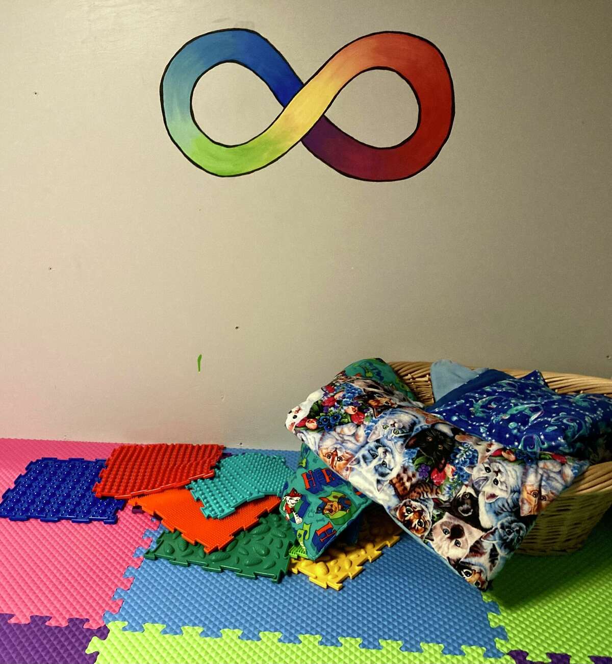 The Calming Corner at Sandcastles Children's Museum includes weighted lap blankets, stuffed animal pillows and an infinity symbol on the wall.