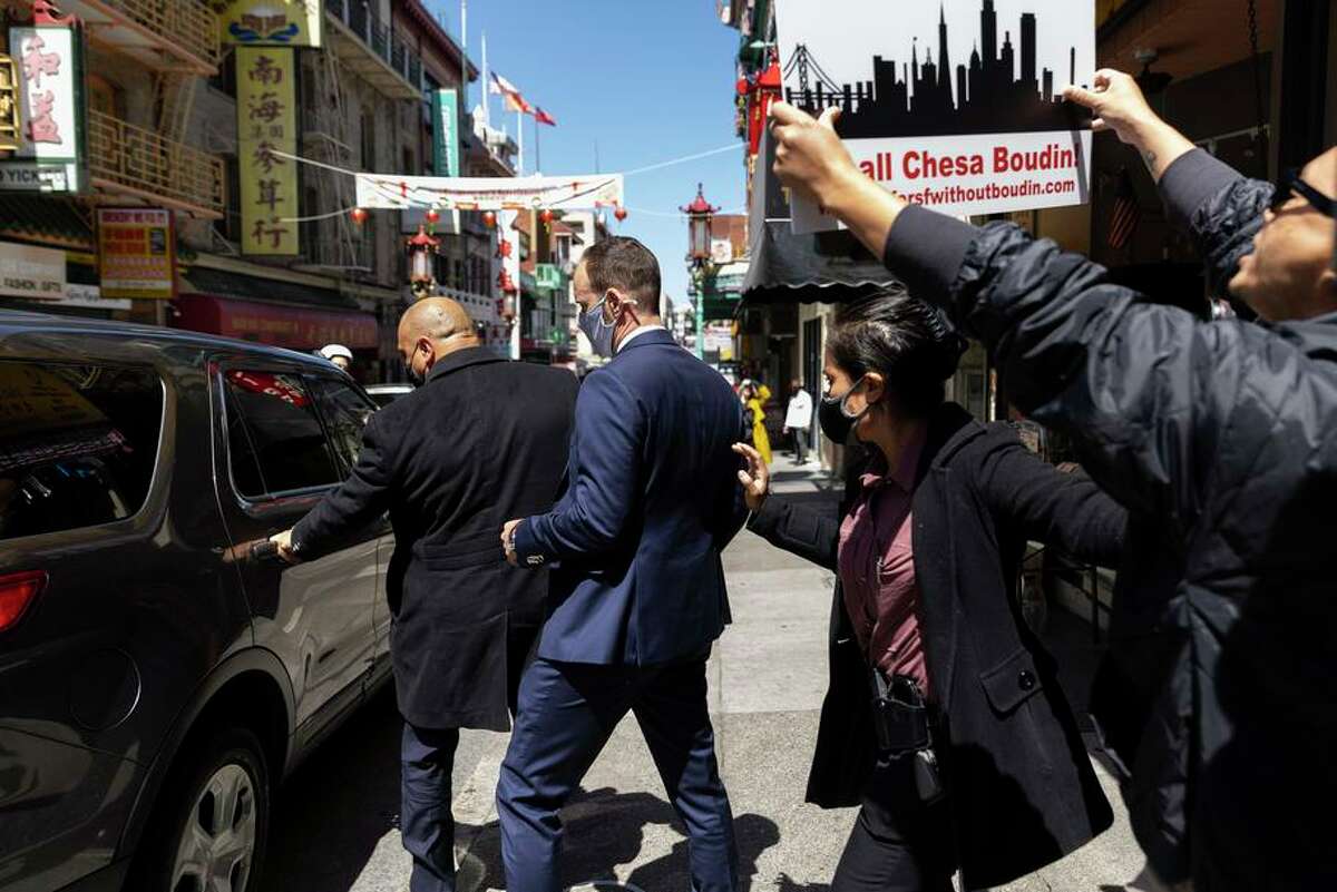 Security guards escort District Attorney Chesa Boudin from a Chinatown event that drew protesters seeking his recall.