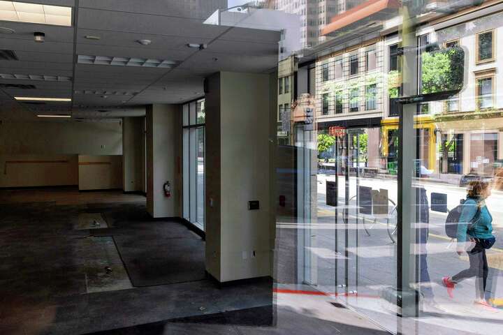 A pedestrian walks past the darkened and emptied interior of a storefront that was once a Walgreens.