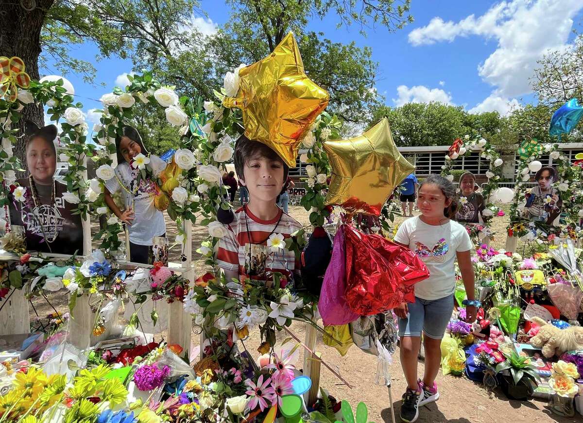A child walks amid flowers and other mementos left in remembrance of the 19 students and two teachers murdered at Robb Elementary School in Uvalde.
