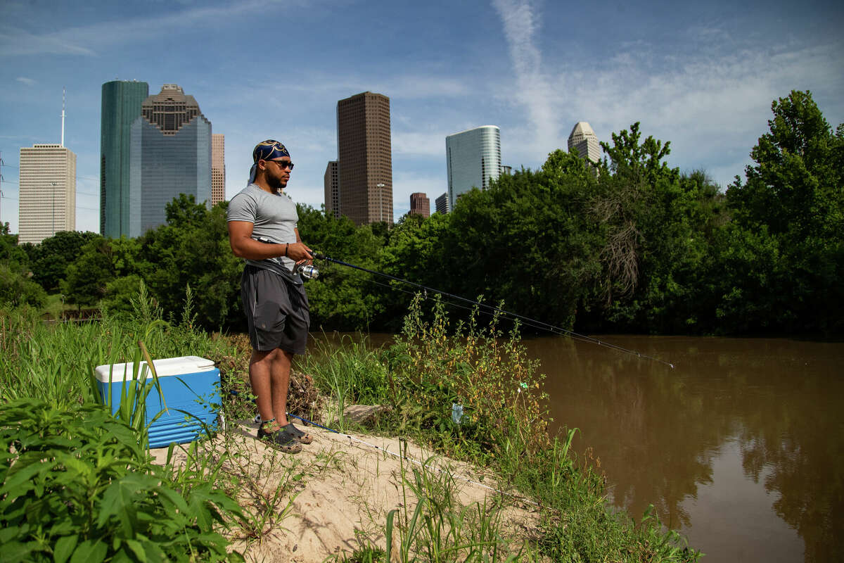 Sean Burns, 20, fishes at the Buffalo Bayou with the skyline of downtown Houston on the background, Tuesday, June 1, 2021, in Houston.