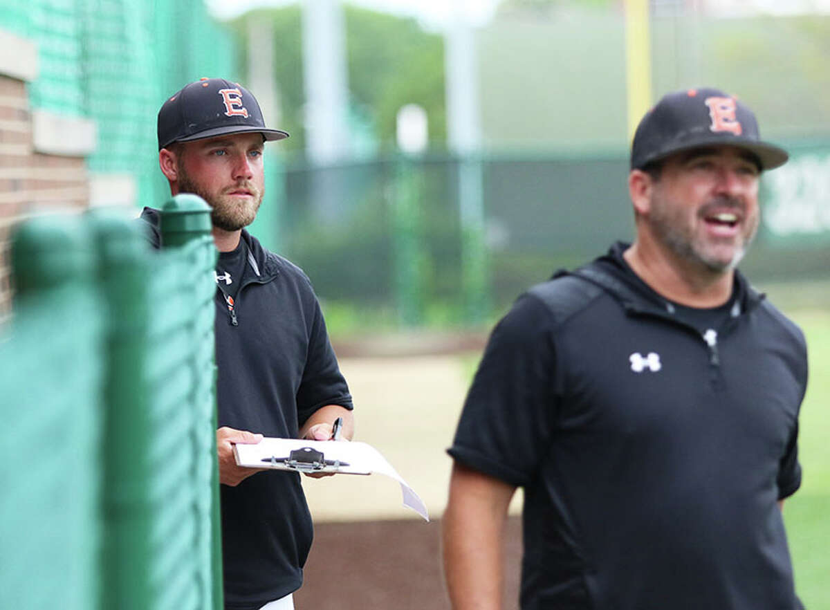 Edwardsville pitching coach Mike Sabatino (left), a 2012 EA-WR graduate, looks on while head coach Tim Funkhouser welcomes Tigers off the field in the middle of an inning against Plainfield North in Monday's Class 4A super-sectional in Bloomington.