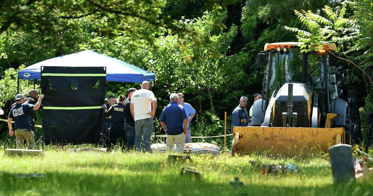 A barrier is moved in front of the casket of what was thought to be an unidentified homicide victim from the 1970s being exhumed at State Street Cemetery in Hamden by the East Haven Police Department on June 8, 2022. It turned out not to be the correct gravesite.