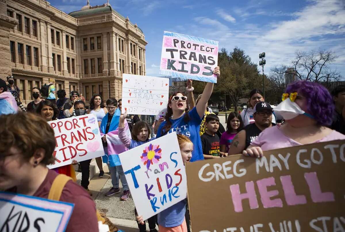 Ashley (middle) chants, “God made trans kids! God loves trans kids!” with her children during a protest at the Texas Capitol on March 1, 2022.
