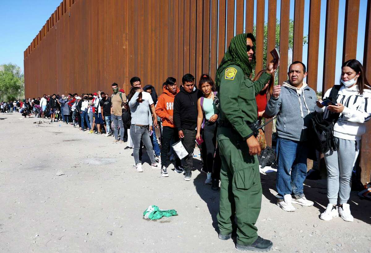 A U.S. Border Patrol agent checks for identification as immigrants wait in line to be processed after crossing from Mexico on May 21, 2022 in Yuma, Arizona.