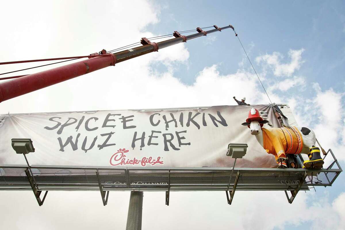Oscar Lugo (top) signals as he and Horica Enciu (bottom) work to remove a Chick-fil-A cow from a billboard near I-10 and Lathrop Street, Wednesday, July 6, 2011, in Houston. ( Michael Paulsen / Houston Chronicle )