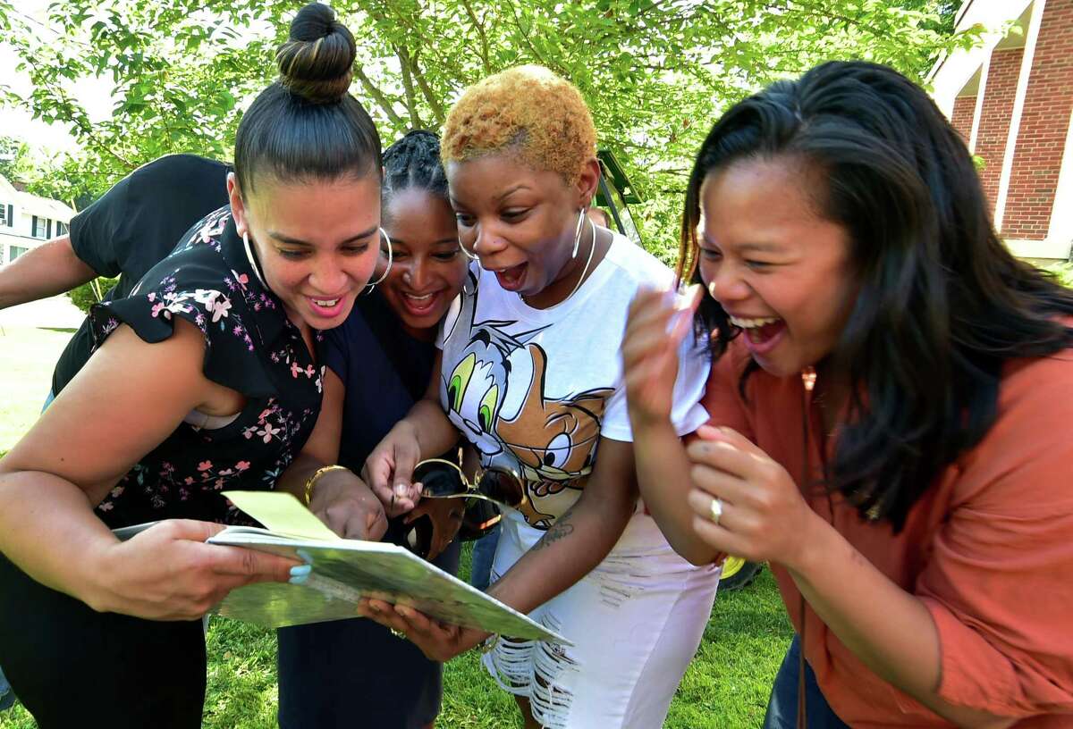Former 7th grade Dolan Middle School students enjoy seeing themselves in a 1997 yearbook as others are digging to find a time capsule from 1997 buried on the school grounds in Stamford, Conn., on Wednesday June 8, 2022. From left to right is Elizabeth Cobbs, Mikelah Rose, Katrina Lomax and Karesia Batan. Westhill High School Principal Michael Rinaldi was a teacher at the school at the time. He had his 7th grade social studies class put together a time capsule to be opened today.