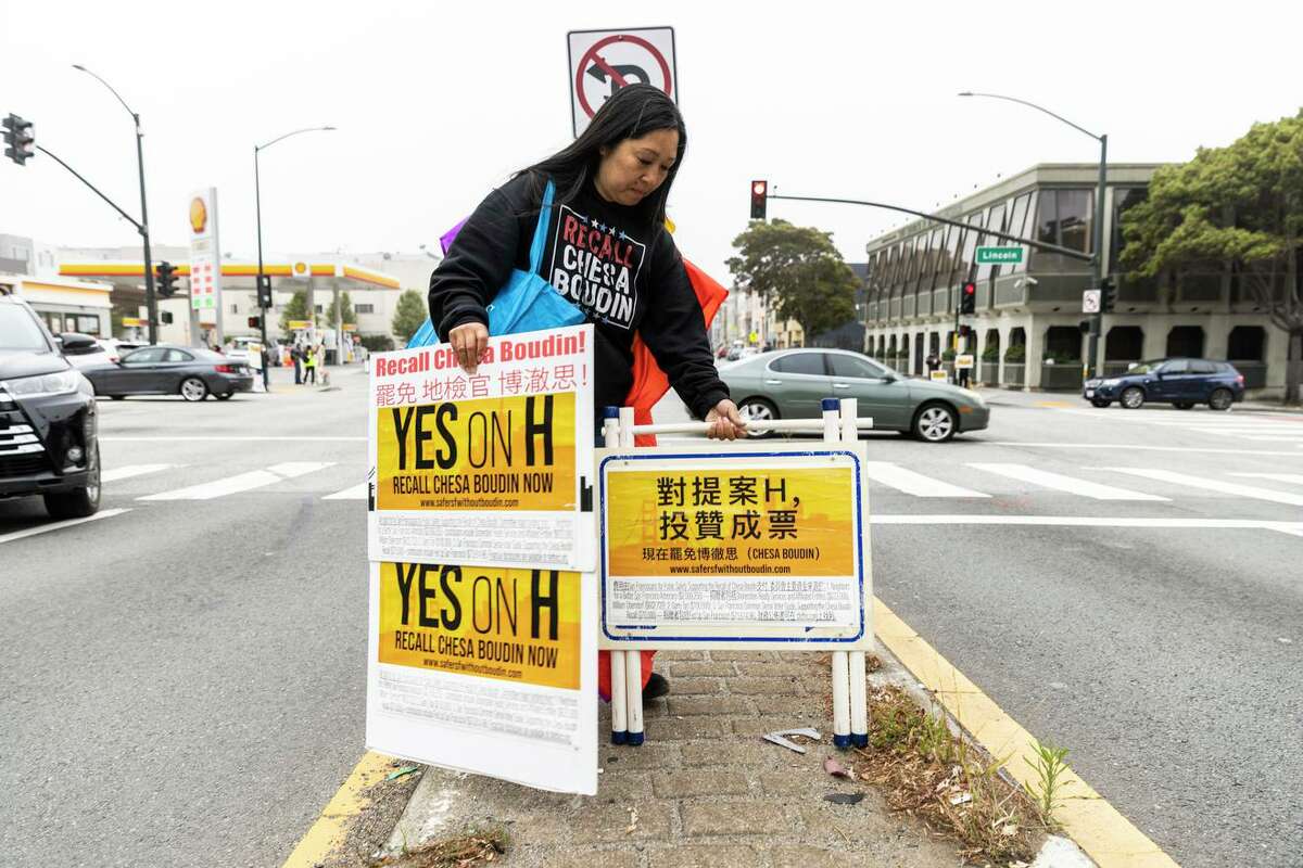 Leanne Louie, a supporter of Proposition H, a ballot measure to recall San Francisco District Attorney Chesa Boudin, places a sign along 19th Avenue in the Sunset District on election day.