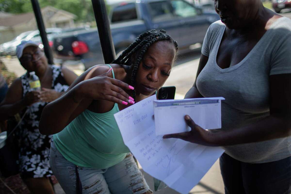 Rose Plaza Apartments resident Lauri Jones, center, 48, takes a look at the handwritten note used as a receipt to document rental payment that was given by the Rose Plaza Apartments administrators to their tenant Joyce Lewis, right, 68.