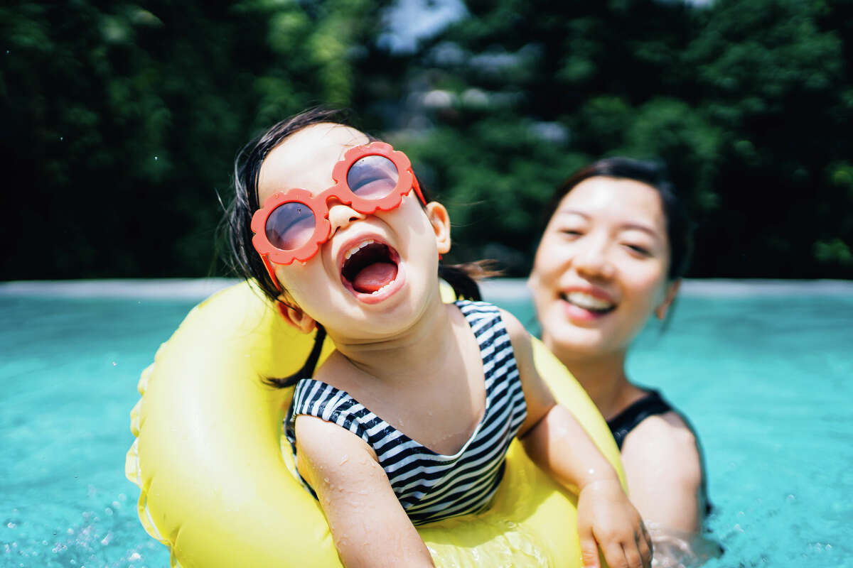 STOCK IMAGE Happy toddler girl with sunglasses having fun in the swimming pool with mom in summer