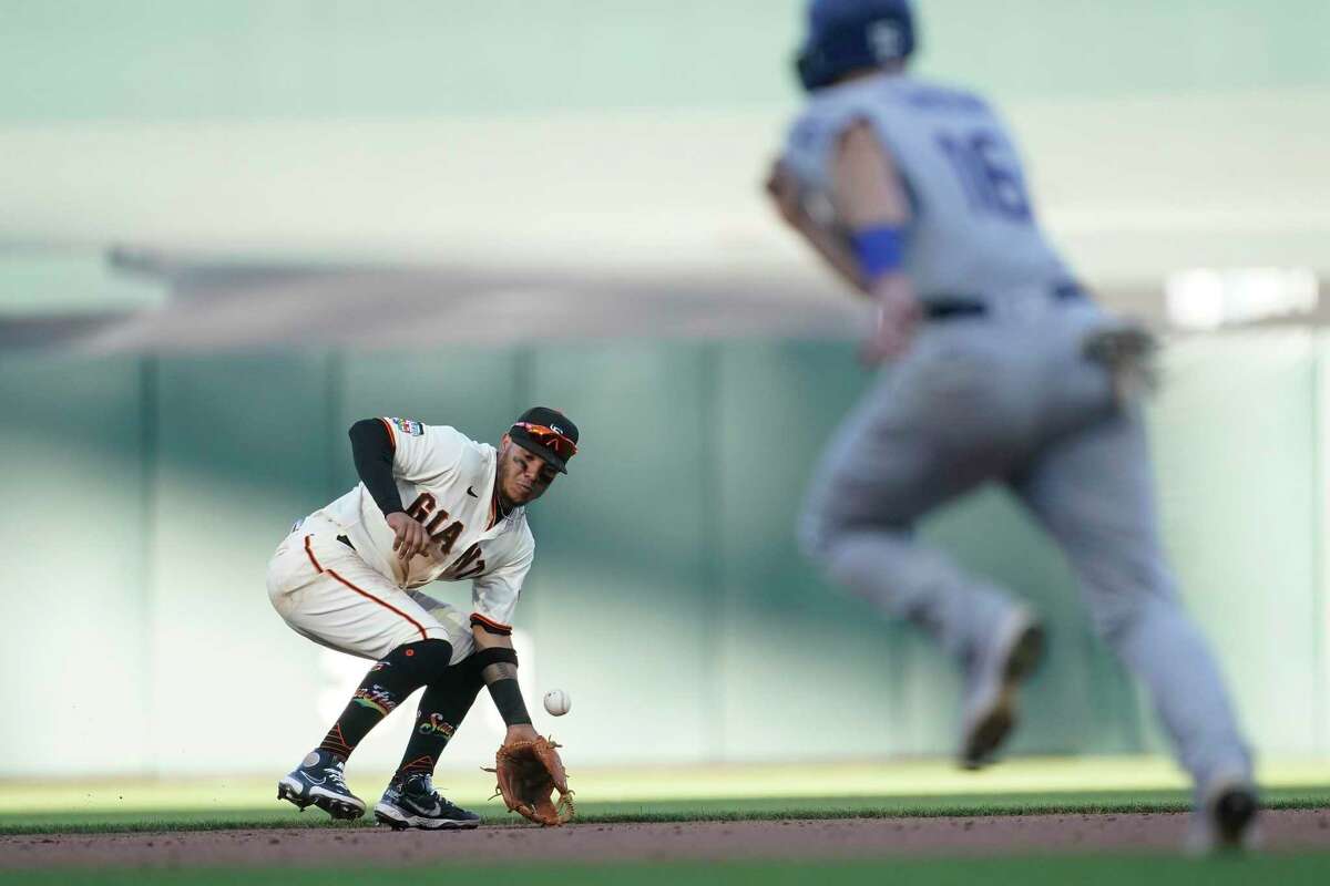 San Francisco Giants second baseman Thairo Estrada, left, makes a fielding error on a ground ball hit by Los Angeles Dodgers' Justin Turner that allowed Will Smith, right, to advance to third base during the eighth inning of a baseball game in San Francisco, Saturday, June 11, 2022. (AP Photo/Jeff Chiu)