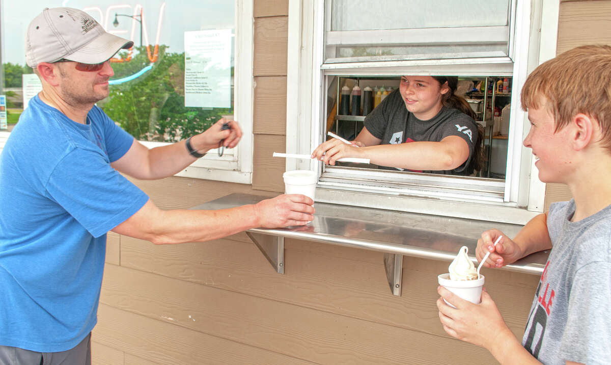 Josh Ayres (from left) gets a cool drink from Jesse Claussen at Charlie's Ice Cream Shop as Josh's son, Nathan, dips a spoon into his ice cream. Nathan was playing at a soccer camp Monday as temperatures moved into the mid-90s. High temperatures of about 97 degrees are expected through much of this week, with heat indices reaching from 105 to 110 degrees.