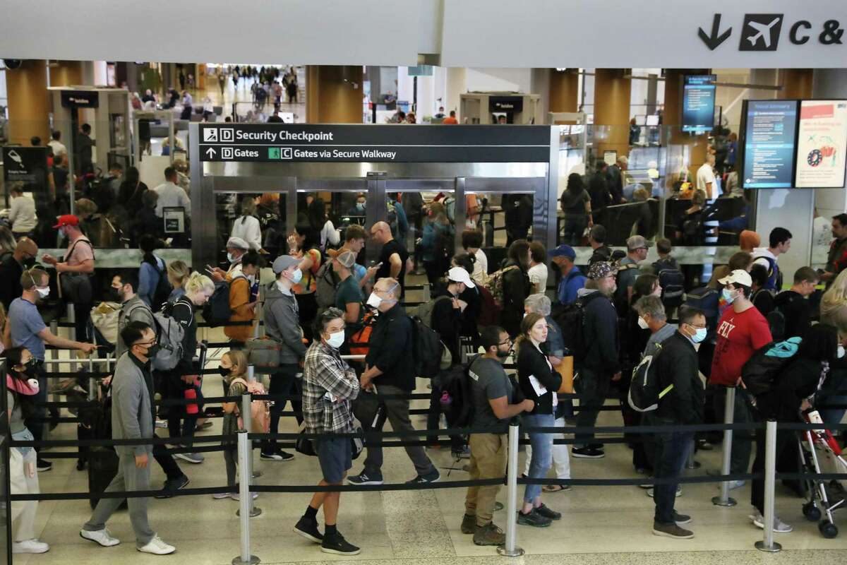 假日旅行增加了新冠病毒再感染的风险。以下是你需要知道的。周三，在旧金山国际机场的一个安检处，人们排起了由柱子组成的长队。