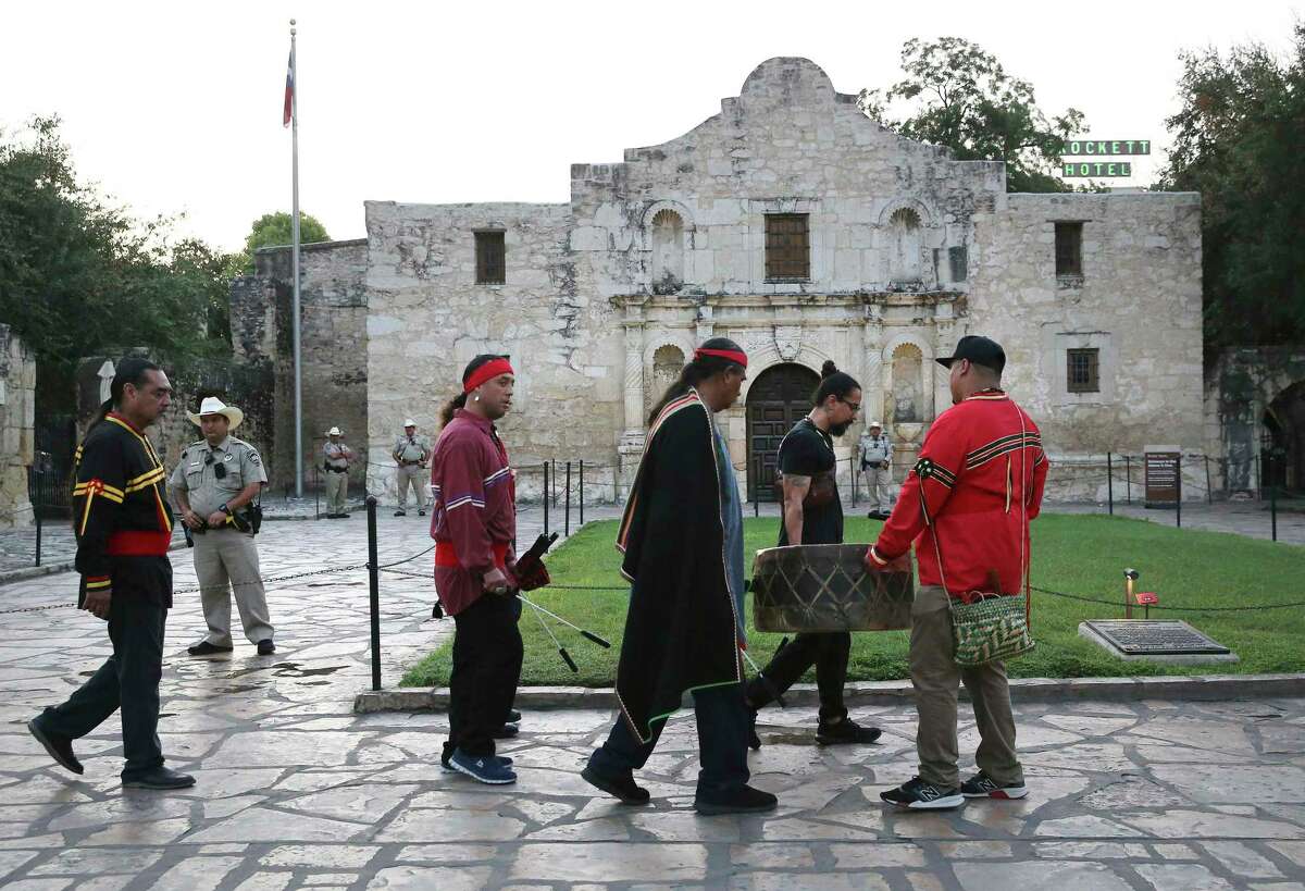 A group of men play a drum as a local Native American pays respect to his buried descendants during his 25th annual sunrise ceremony at the Alamo on Saturday, Sept. 7, 2019. Ramon Juan Vasquez (pictured left), executive director of American Indians in Texas at the Spanish Colonial Missions, along with more than 60 people who claim ancestry with the native Indians who are buried on the grounds of the Alamo, formed a circle outside the church to pray and honor their descendants.  In the past, the group was allowed to have the service inside the chapel, but were told days before the event that the service would not be allowed inside the Alamo.  With a noticeable presence of Alamo security guards and a chain blocking the march to the front doors, the group formed a circle in Alamo Plaza to air their grievances and remember their descendants.  Vasquez and the group were joined by State Senator Jose Mendendez, State Representative Leo Pacheco and Poet Laureate Carmen Tafolla who all expressed dismay that the indigenous group is not allowed to pray and honor their loved ones. inside the Alamo.  Despite the ban, members of the Tap Pilam Coahuiltecan Nation and other Indigenous peoples paid their respects on the grounds in front of the Alamo.  A sage-filled shell burned slowly and filled the early morning sky with puffs of smoke — traditionally used to bless and purify — as the service ended just as the sun rose over the Alamo.  (Kin Man Hui/San Antonio Express-News)