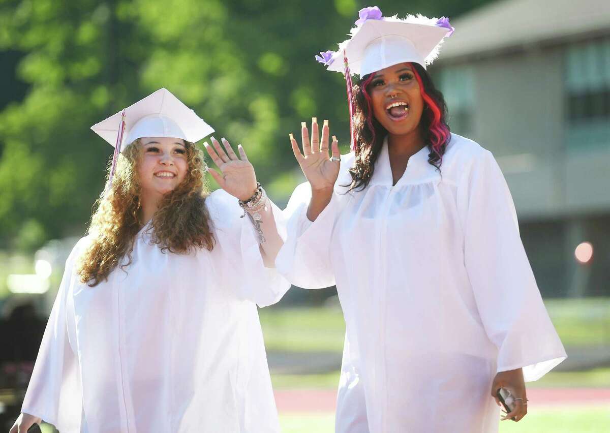 Dominika Rembowska, left, and Aaliyah Hicks wave to family in the stands as they walk in with their classmates to the Derby High School graduation on Tuesday.
