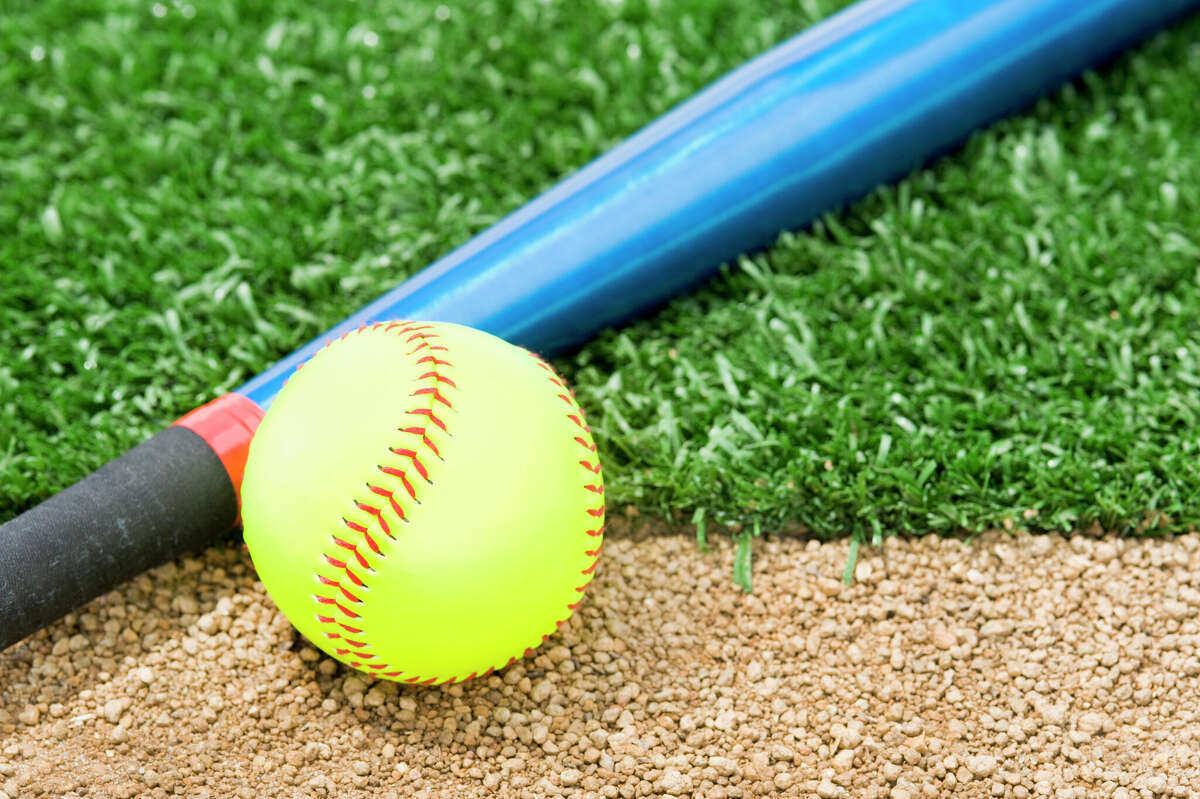 A New "Fast Pitch" Softball and an aluminum bat sitting between the infield grass and dirt of a softball diamond