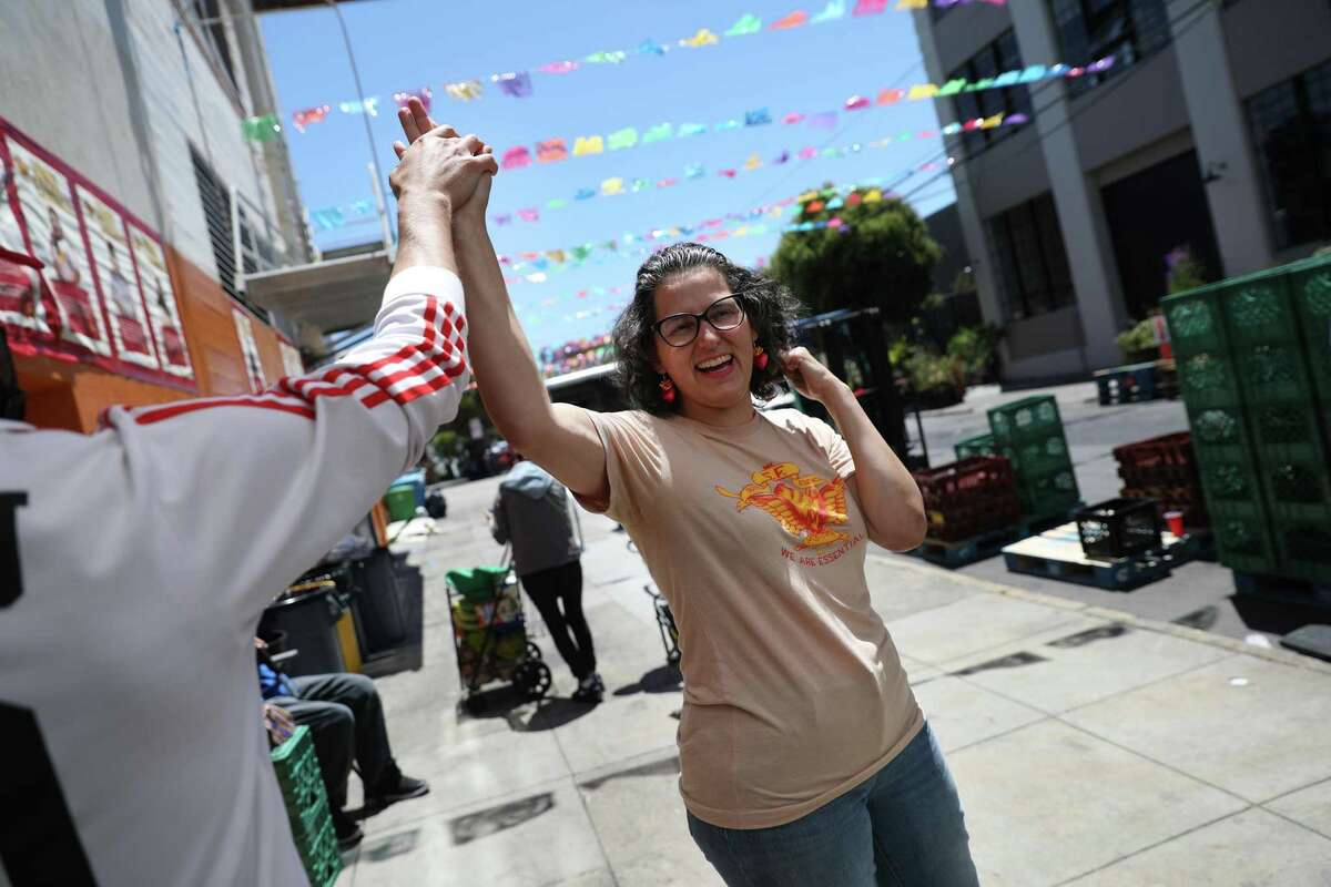 Adriana Camarena, researcher and lead facilitator, high fives a volunteer on Alabama Street at the Mission Food Hub who was reacting from a score in the World Cup on Monday, June 13, 2022 in San Francisco, Calif.