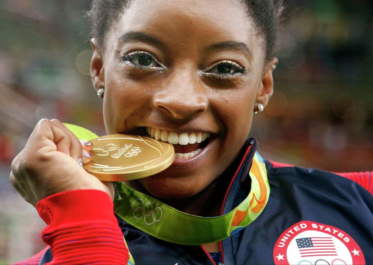 United States' Simone Biles bites her gold medal for the artistic gymnastics women's individual all-around final at the 2016 Summer Olympics in Rio de Janeiro, Brazil, Thursday, Aug. 11, 2016.