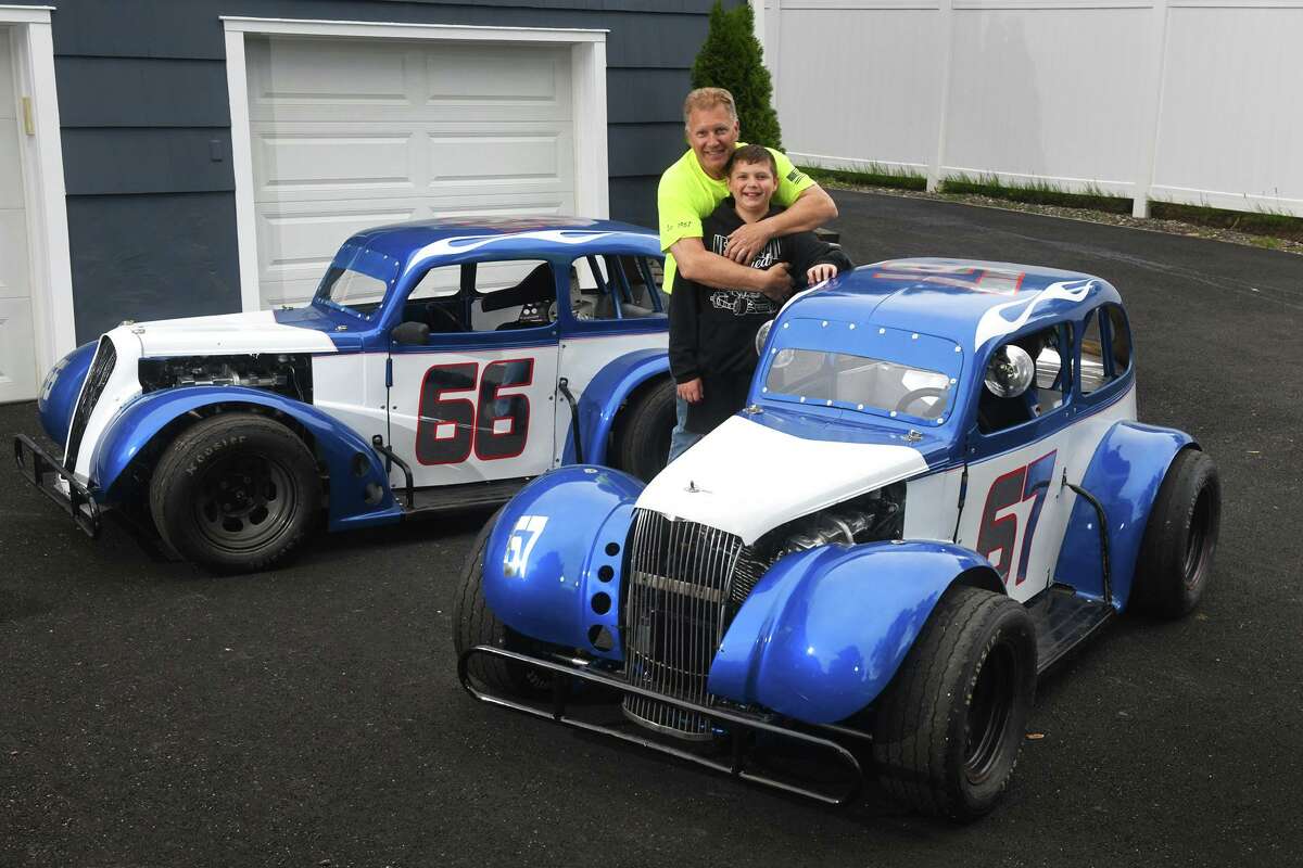 Ron Miske and his son, Tyler, 12, pose next to their Legend series race cars in front of their home in Shelton, Conn. May 19, 2022.