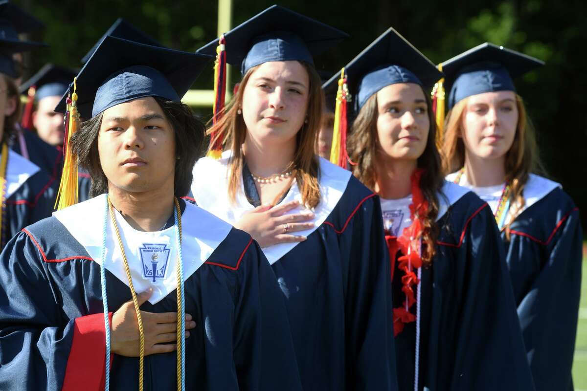 Above, Jay Yang, left, stands with fellow classmates for the national anthem during graduation at Foran High School in Milford on Friday. Below, Layla Carlberg adjusts her cap during the ceremony.