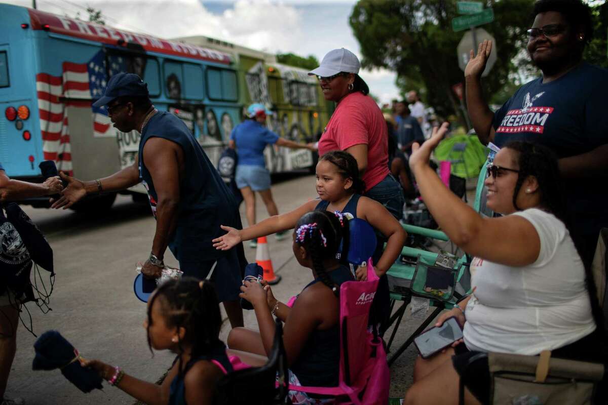 The Jenkins family wave toward a Freedom Riders bus and receive swag from employees of the City of Houston participating in the Mayor Turner's 9th Annual Juneteenth Parade, Saturday, June 18, 2022, in Houston.