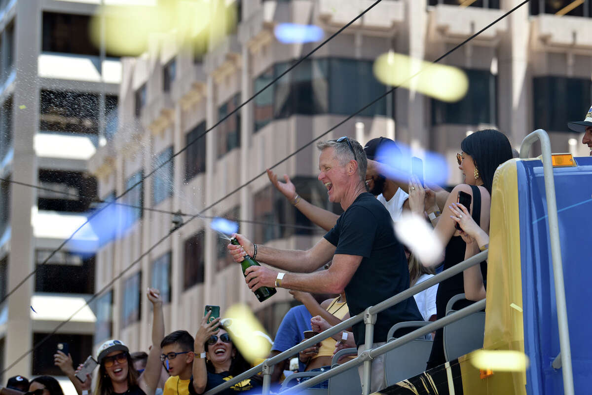 Warriors head coach Steve Kerr opens a bottle of champagne from atop his bus during the team's victory parade down Market Street, on Monday, June 20, 2022. 