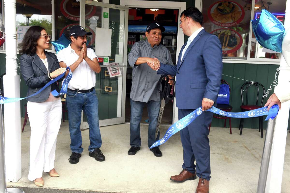 Mayor Ben Blake shakes hands with co-owner Toni Quintero during a ribbon cutting ceremony at Isabel's Bakery and Restaurant, in the Devon neighborhood of Milford, Conn. June 7, 2022. Blake and Quintero are seen here with Marisol Herrera of the Hispanic Chamber of Commerce of Greater Bridgeport and co-owner Emiliano Dominguez.