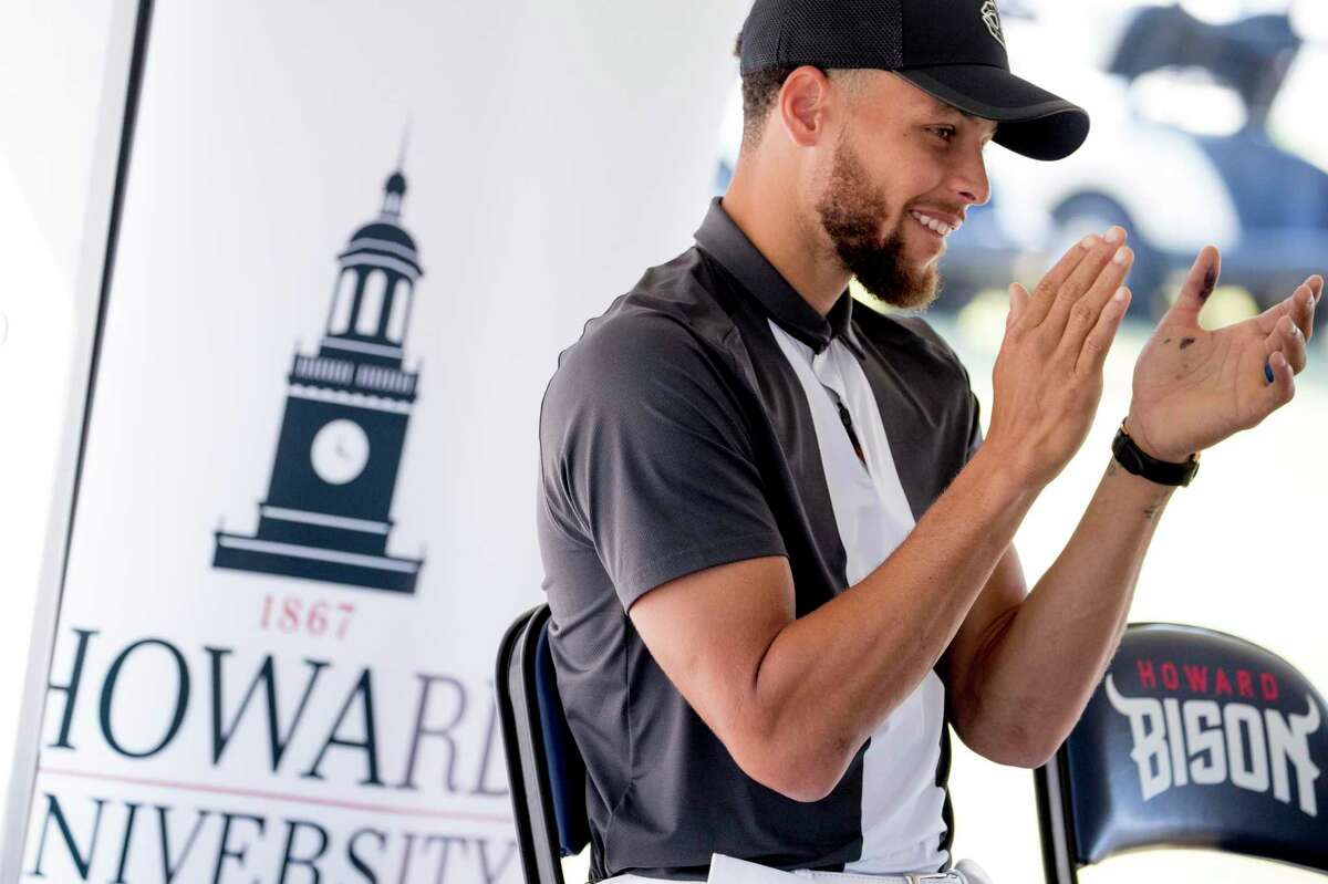 The Howard University logo is visible behind Warriors guard Stephen Curry as he applauds during a news conference at Langston Golf Course in Washington on Aug. 19, 2019. Curry announced he would be sponsoring the creation of men’s and women’s golf teams at Howard.
