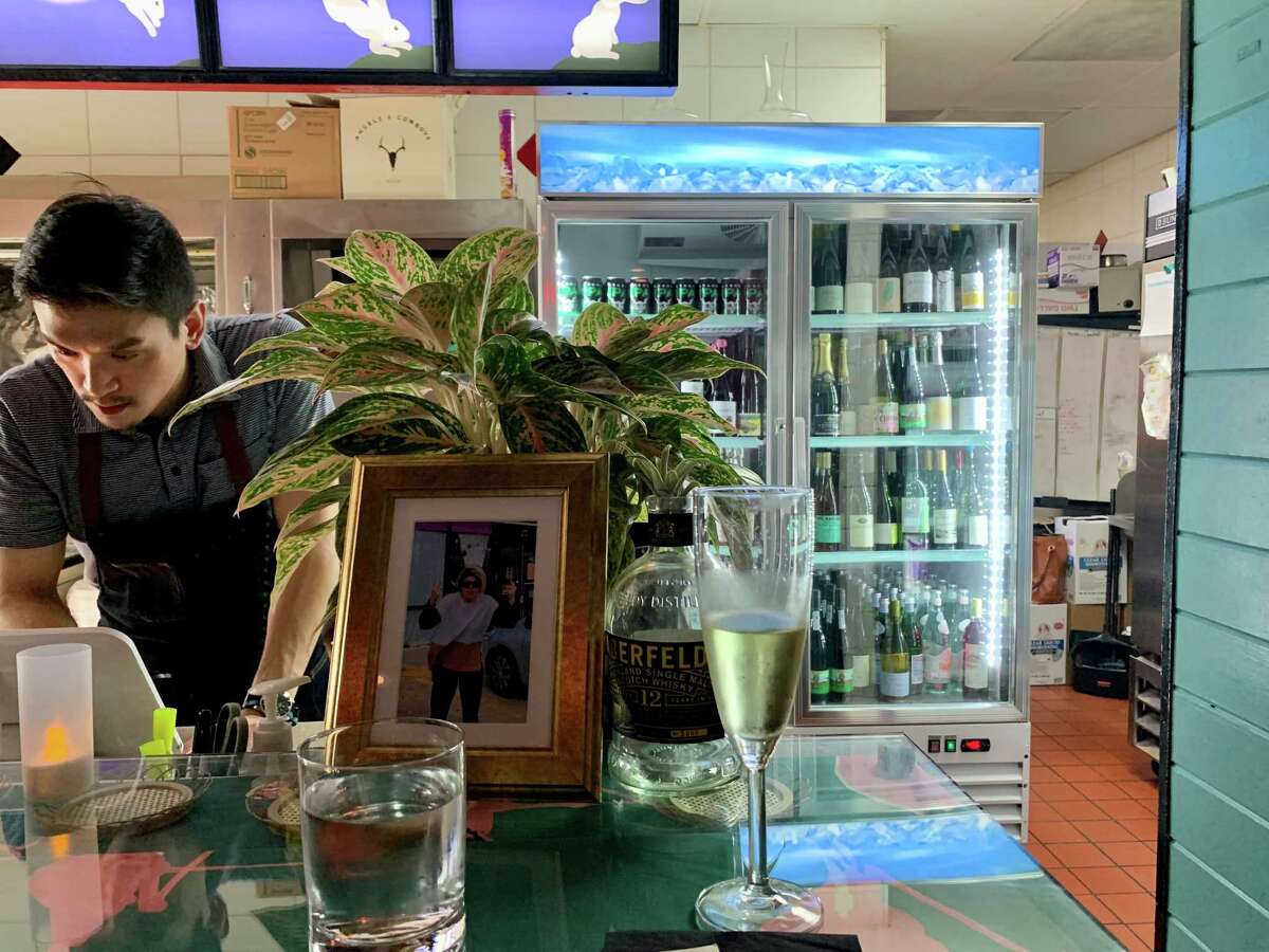 El mostrador de cuatro asientos en el restaurante Street to Kitchen Thai tiene vista al nuevo enfriador de vino y cerveza y un mural iluminado de conejos blancos.