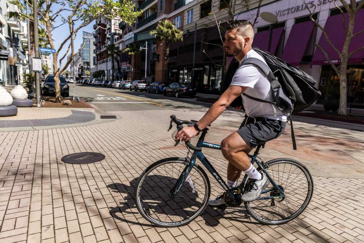 Emeryville Mayor John Bauters commutes on a bicycle along Bay Street to return two tuxedo rentals in Emeryville, California Friday, March 18, 2022. Located between larger cities Berkeley and Oakland, the city of Emeryville has been pushing to make it more livable on many fronts including more affordable housing and various cycling infrastructure.