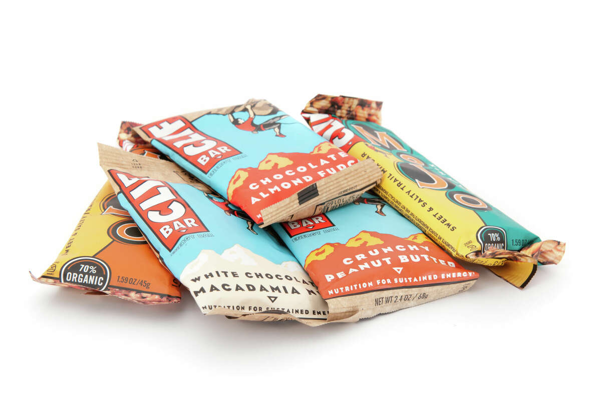 A pile of Clif Bars and Clif Mojo Energy Bars manufactured by Clif Bar & Company sits isolated on a white background. 