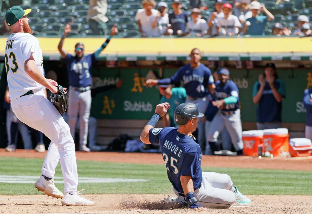 The Mariners’ Dylan Moore scores on a wild pitch by Athletics pitcher A.J. Puk (left) to tie the game 1-1 in the ninth inning.