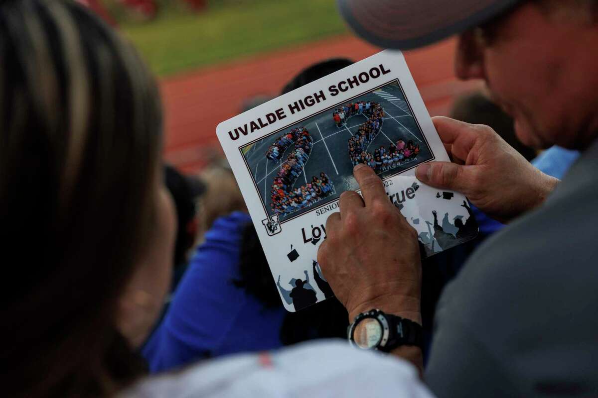 People attending the Uvalde High School graduation ceremony point out graduates in a Class of 2022 class picture that was printed on laminated fans, Friday evening, June 24, 2022. The fans were handed out to combat the 100 degree heat.