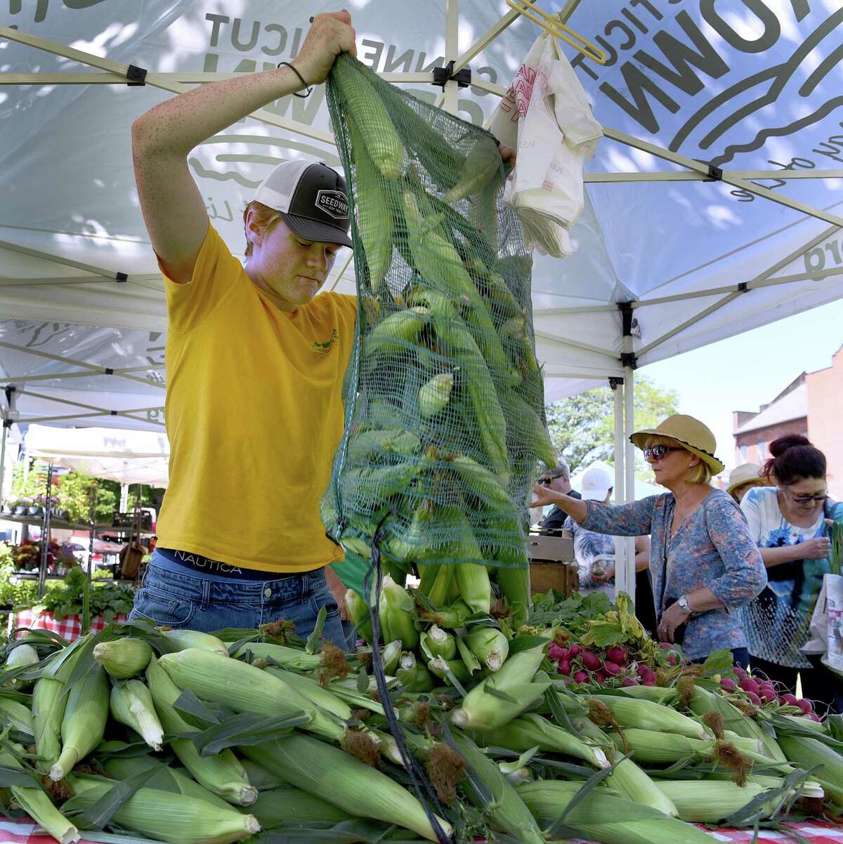 Aidan Schulz adds more fresh corn to Clatter Valley Farm's booth at the Danbury Farmers Market on Saturday morning. The market opened for the season in a new location, the CityCenter Green, Saturday, June 25, 2022.