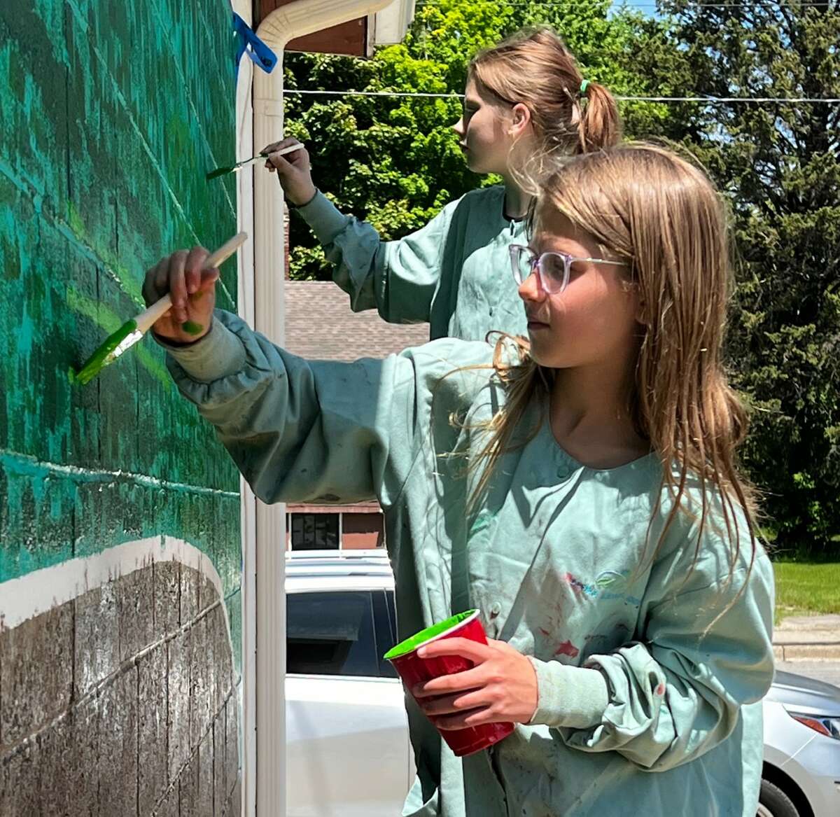 Hazel Sedelmaier (front) and Dannika Berensten paint a section of the mural at the Farr Center in Onekama.