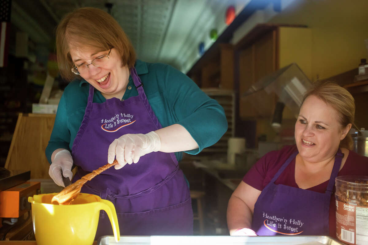Heather 'n Holly employee Melissa Brubaker, right, watches as Midland Daily News reporter Victoria Ritter, left, tries her hand at making chocolate and caramel-covered pretzel sticks Monday, June 27, 2022 at the store in downtown Midland.