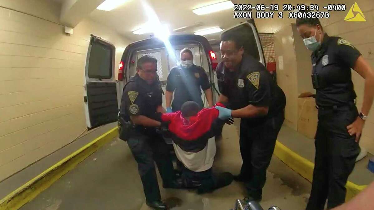 In this frame taken from police body camera video, Richard Cox, center, is placed in a wheel chair after being pulled from the back of a police van after being detained by New Haven Police, June 19, 2022, in New Haven, Conn.