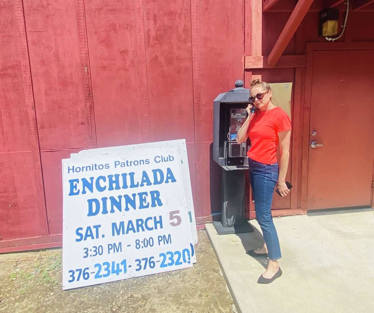 A woman pretends to use a payphone next to a sign for Hornitos' annual enchilada dinner.